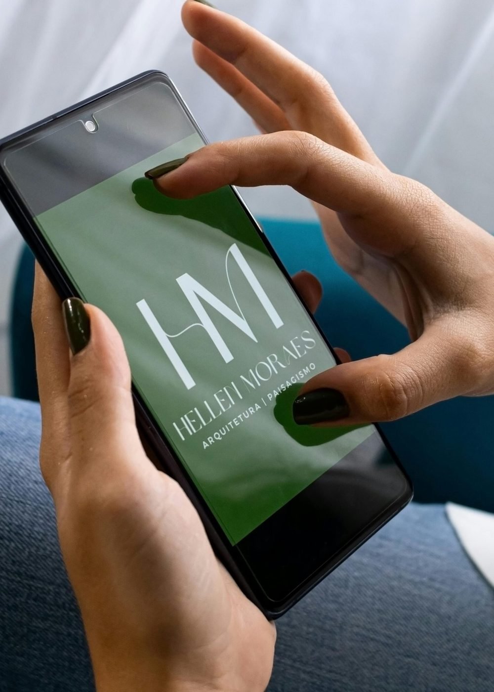 Close-up of hands holding a smartphone with Hellen Moraes logo, showing design and branding concept.